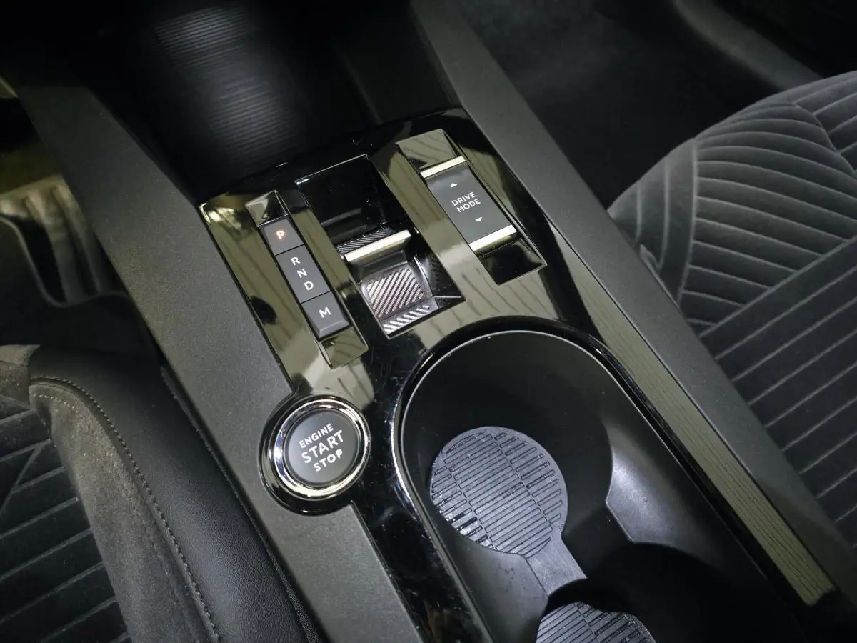 Vue rapprochée de la console centrale noire brillante de la Lancia Ypsilon 2025 avec bouton start/stop et commandes de boîte auto.