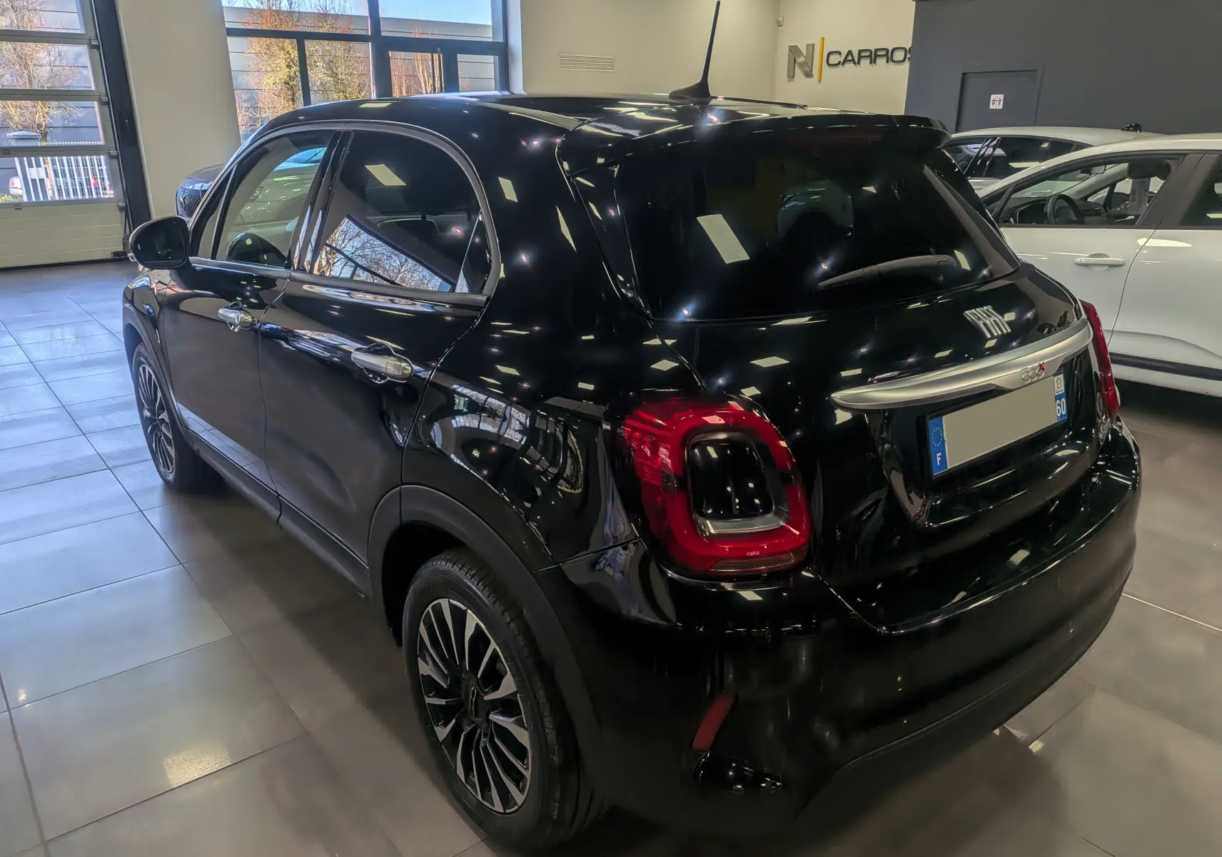 Vue 3/4 arrière droite d'une Fiat 500X noire Cinéma 2024 en intérieur, avec feux arrière distinctifs et jantes bi-ton.