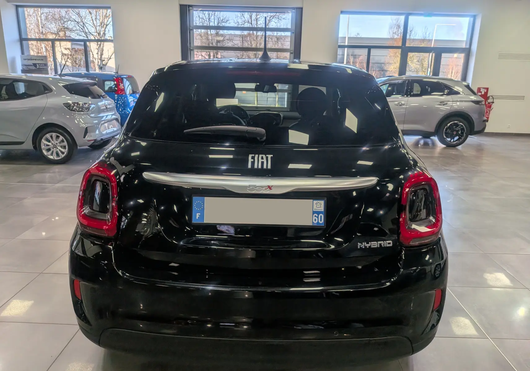 Vue arrière d'une FIAT 500X hybride noire Cinéma avec feux arrière rouges et logo Hybrid visible en concession.