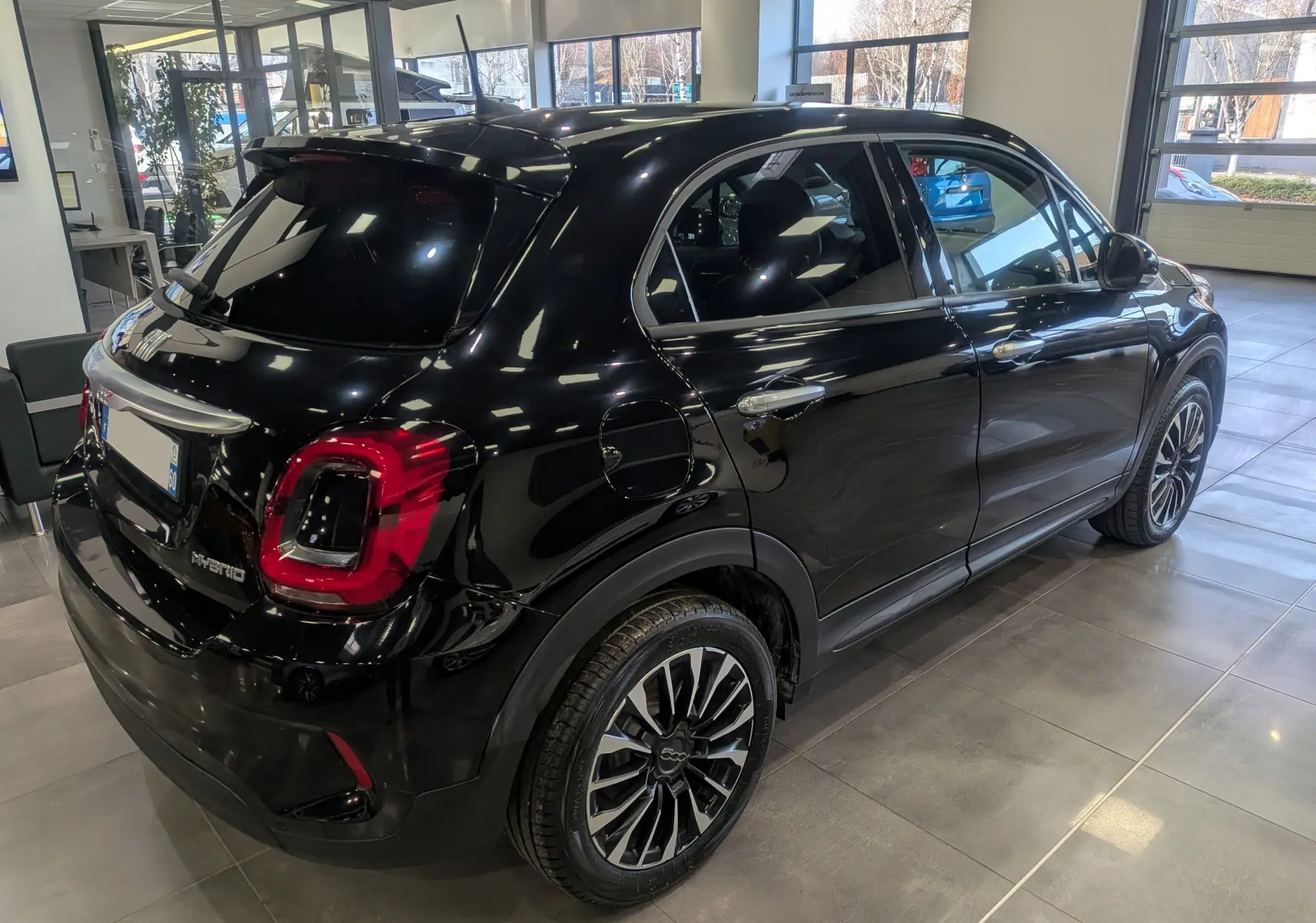 Vue 3/4 arrière droite de la FIAT 500X 2024 noire Cinéma, hybride essence, avec jantes alliage bicolores et feux arrière LED.