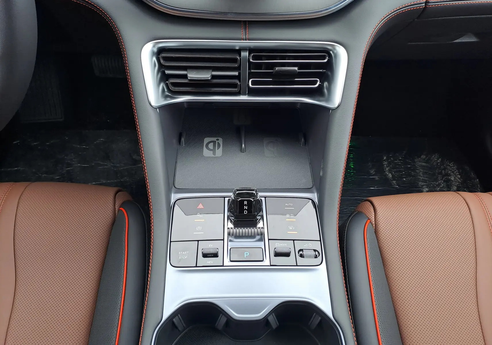 Vue plongeante sur la console centrale argentée du BYD SEAL U avec sièges marron et surpiqûres orange visibles.