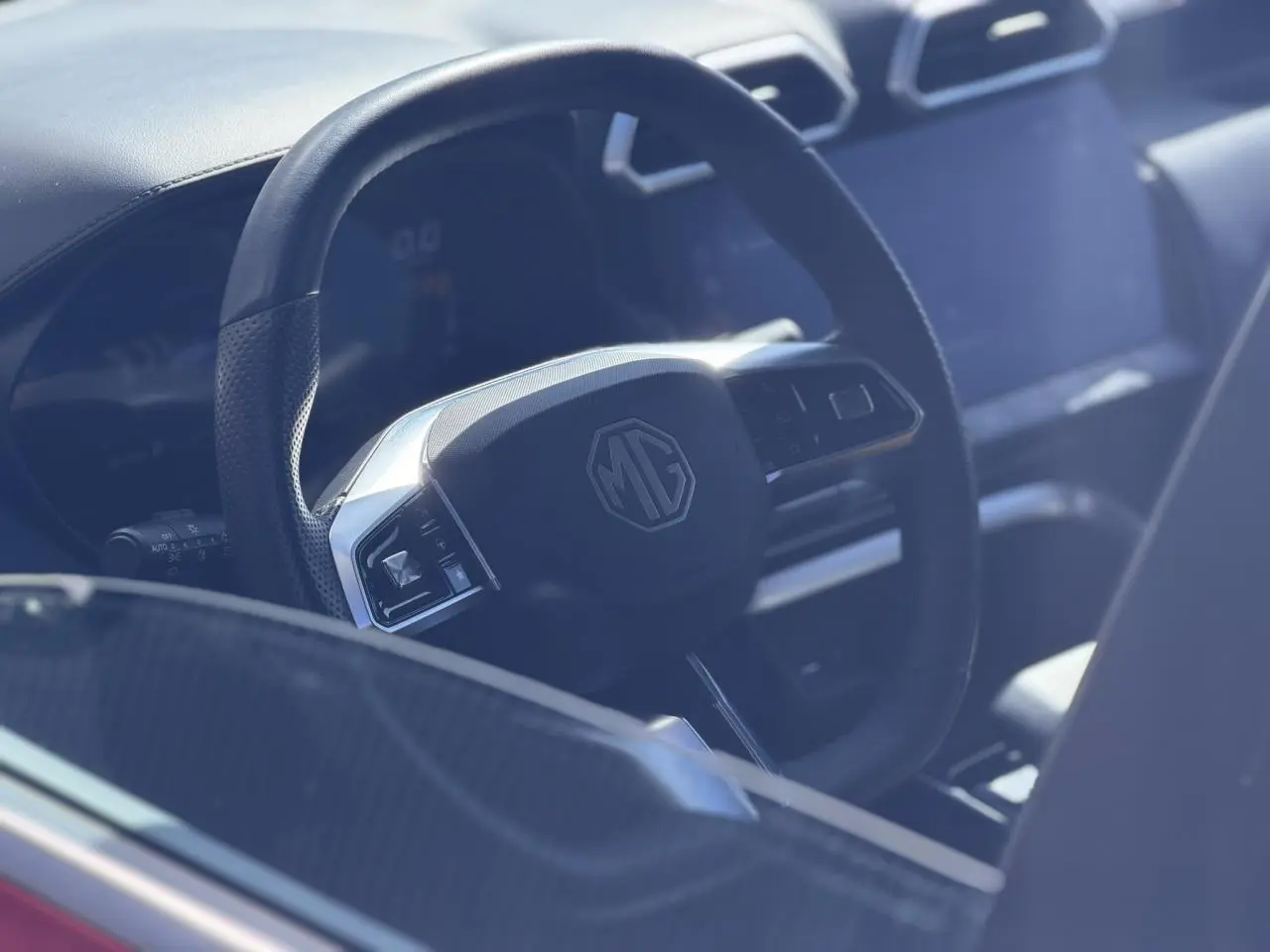 Gros plan sur le volant en cuir noir du MG ZS 1.5 Hybrid+ 197 Luxury avec tableau de bord et écran tactile visibles.