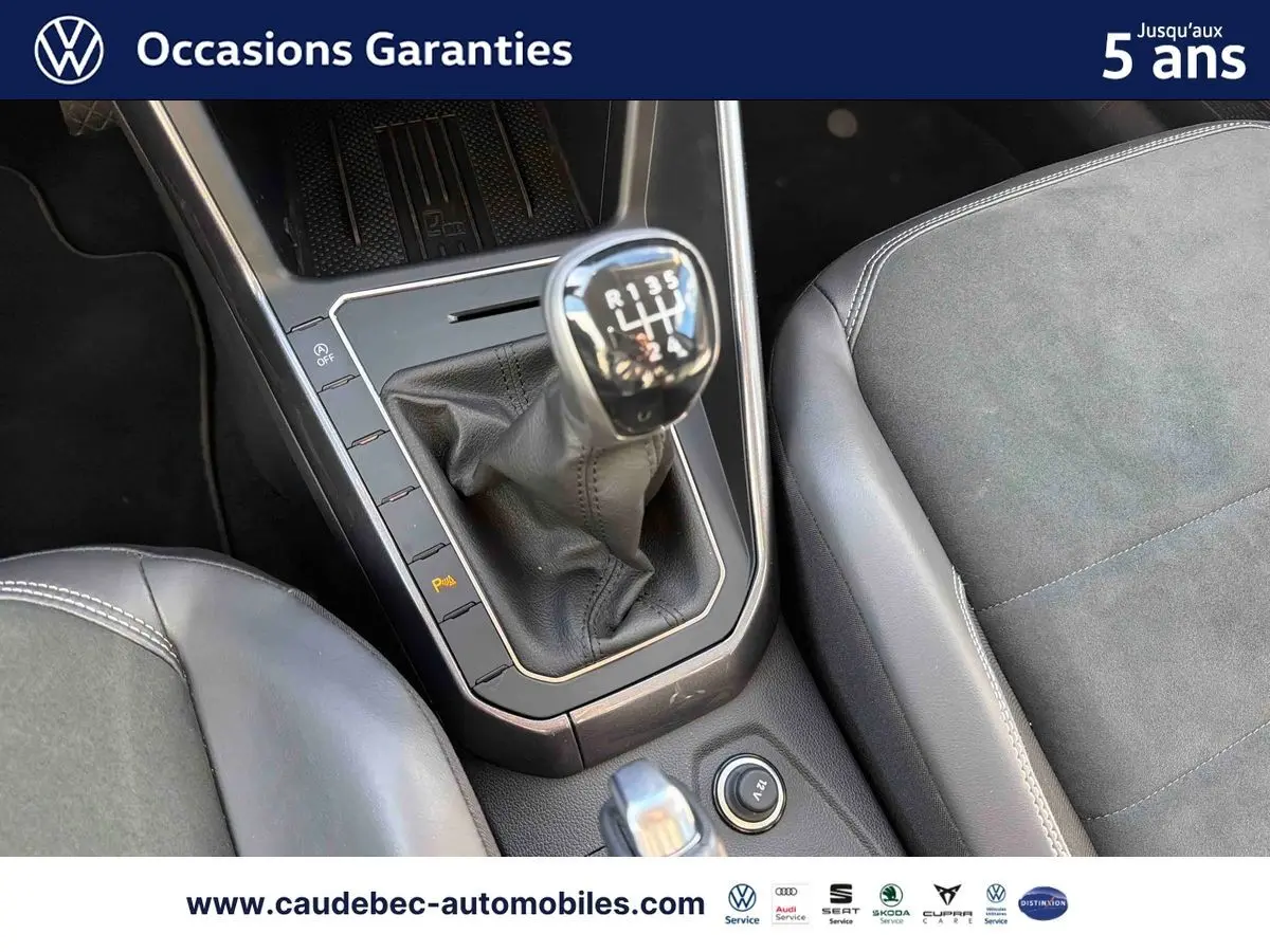 Gros plan sur la console centrale avec levier de vitesse manuel et sièges en cuir et alcantara gris d'une Volkswagen Polo noire.