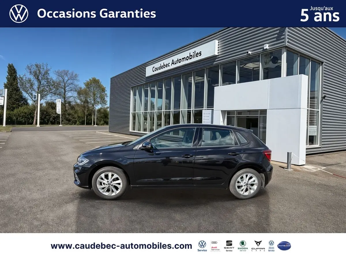 Vue de profil côté gauche d'une Volkswagen Polo 2025 noire intense nacrée, stationnée devant un bâtiment moderne de concession.