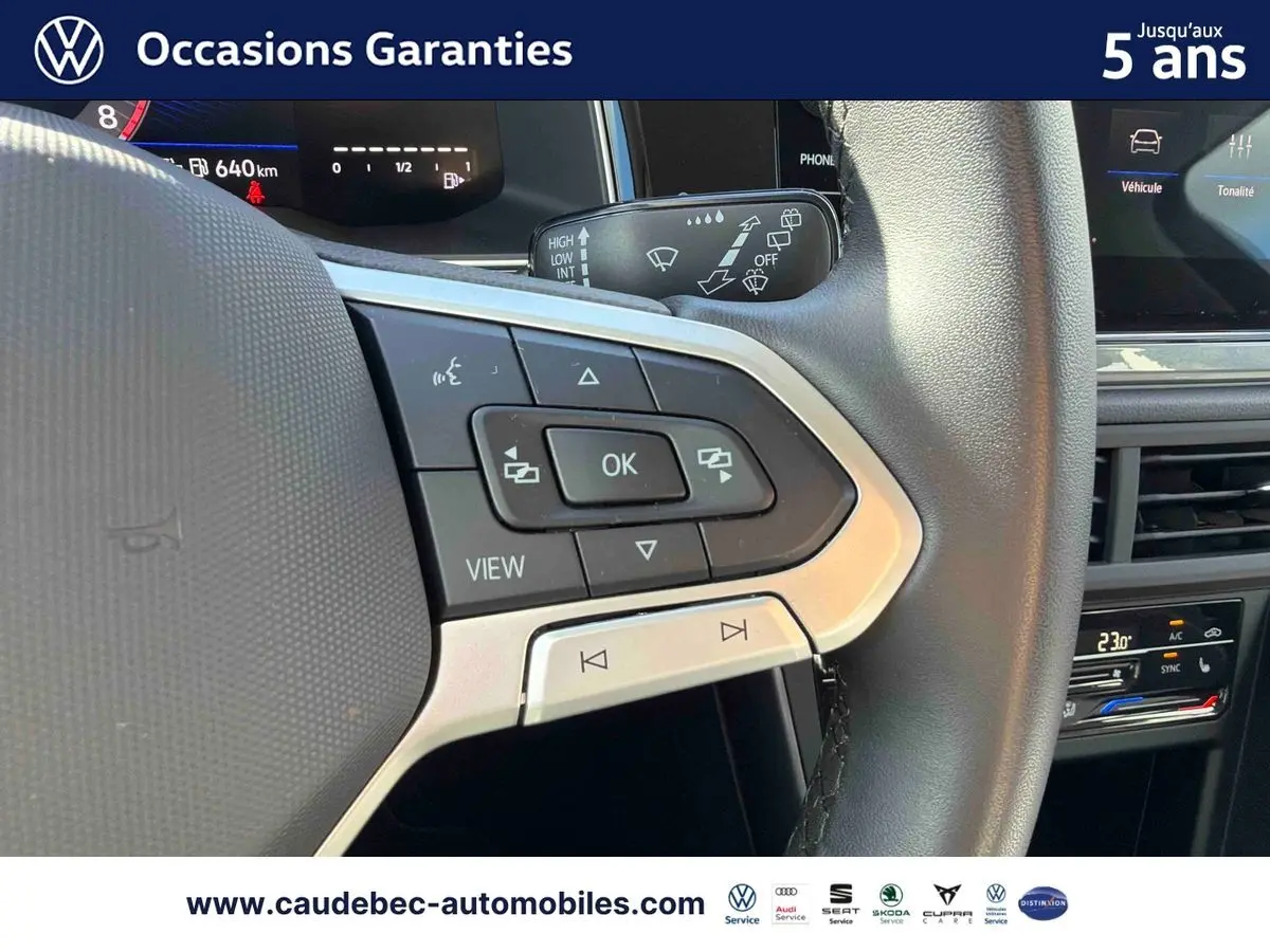 Gros plan sur les commandes au volant cuir de la Volkswagen Polo noire, avec écran digital et climatisation visible en arrière-plan.