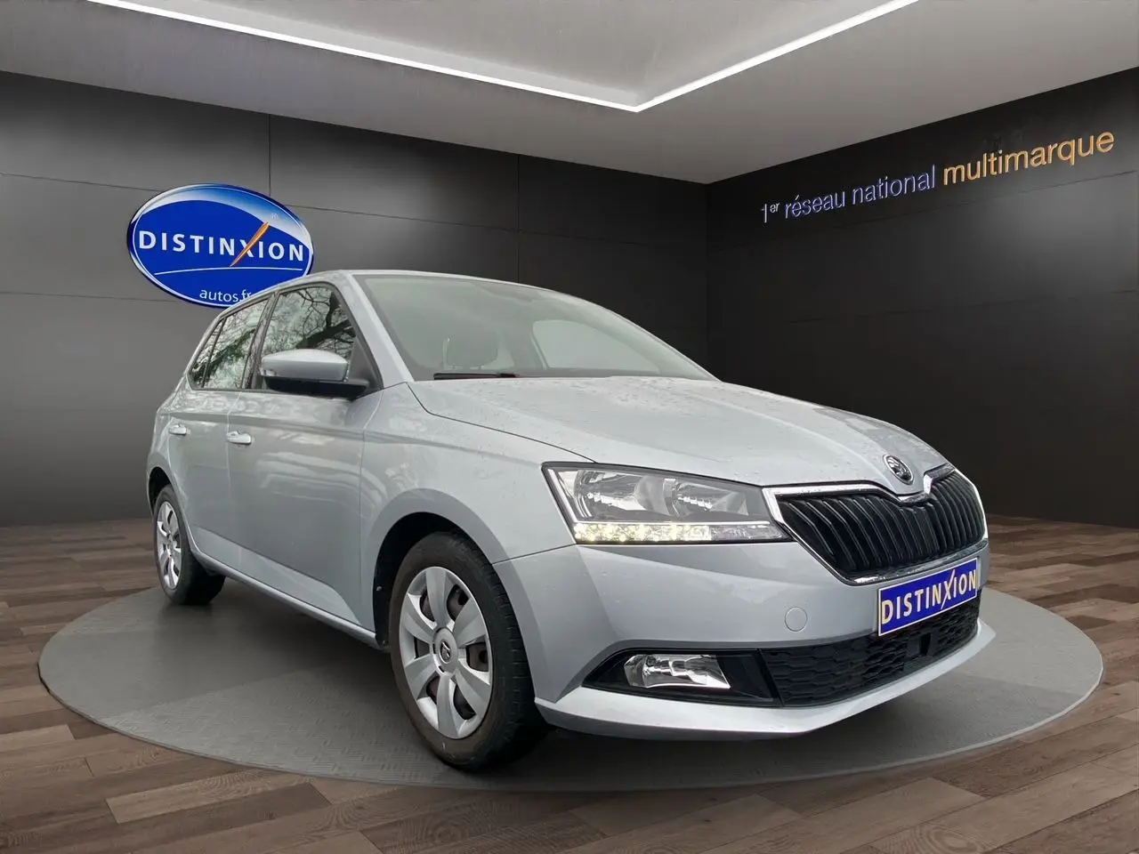 Vue 3/4 avant d’une Skoda Fabia gris argent 2021 avec calandre noire et feux LED allumés en intérieur showroom.