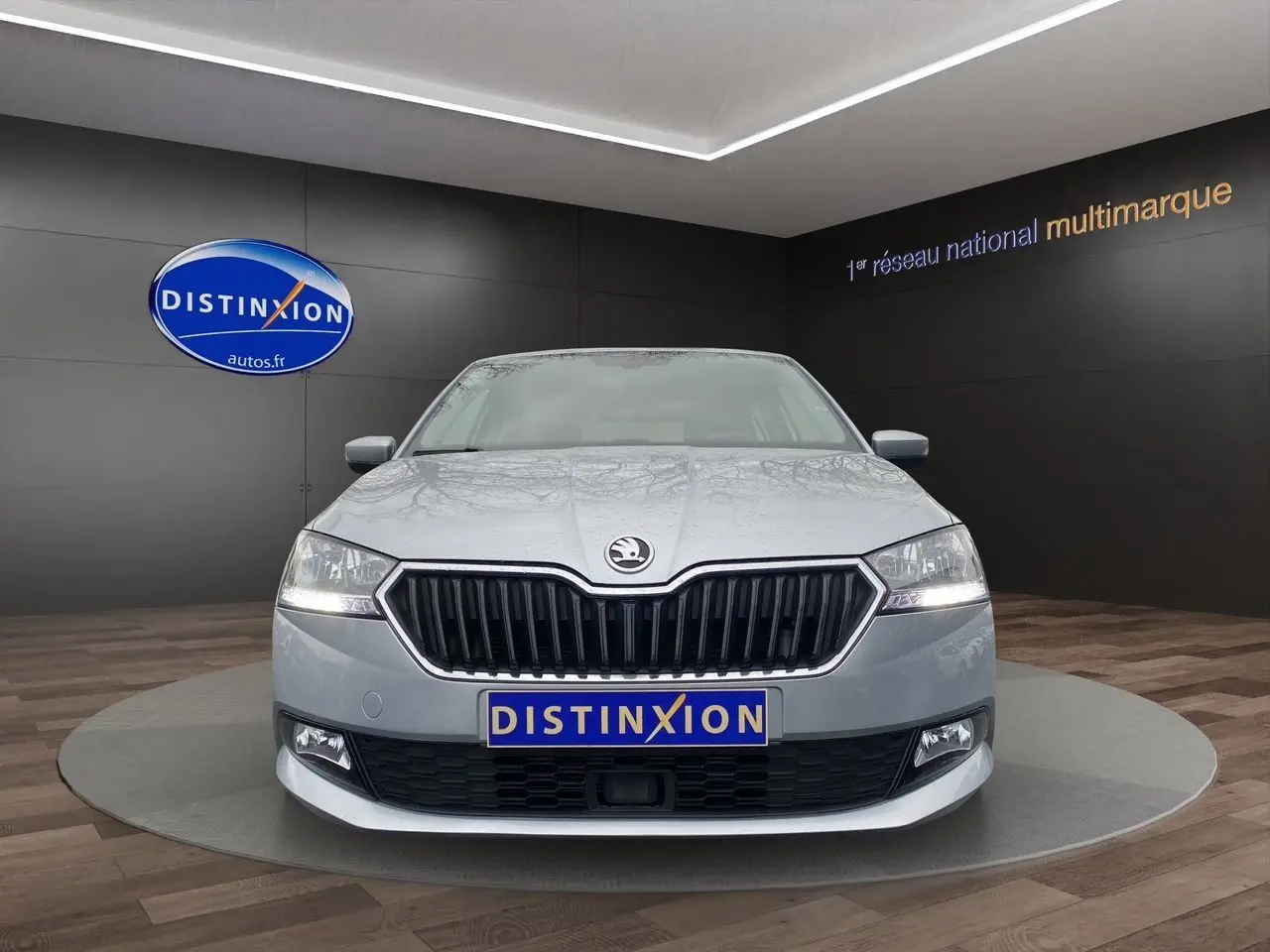 Vue avant d'une Skoda Fabia gris argent 2021 avec calandre noire et phares allumés en showroom.