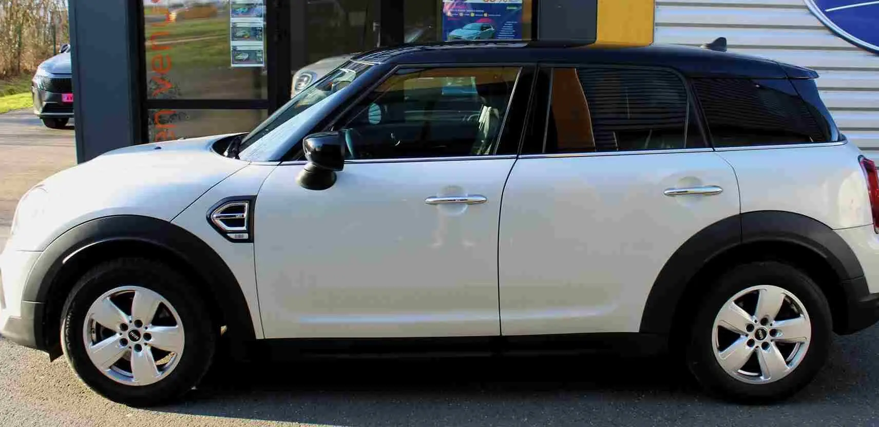 Vue de profil droit d'un MINI Countryman gris perle métallisé avec toit noir, jantes alliage et protections noires sur passages de roues.