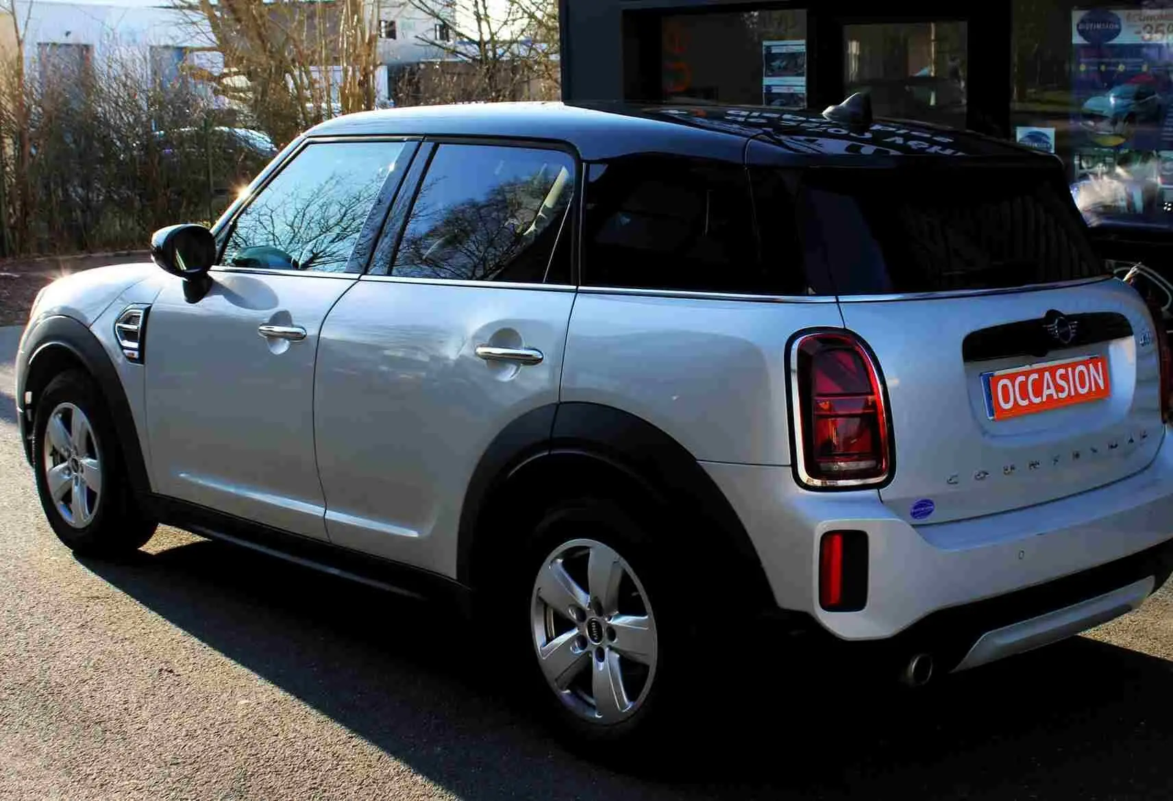 Vue 3/4 arrière droite d'un MINI Countryman gris perle métal avec toit noir, en stationnement devant un bâtiment.