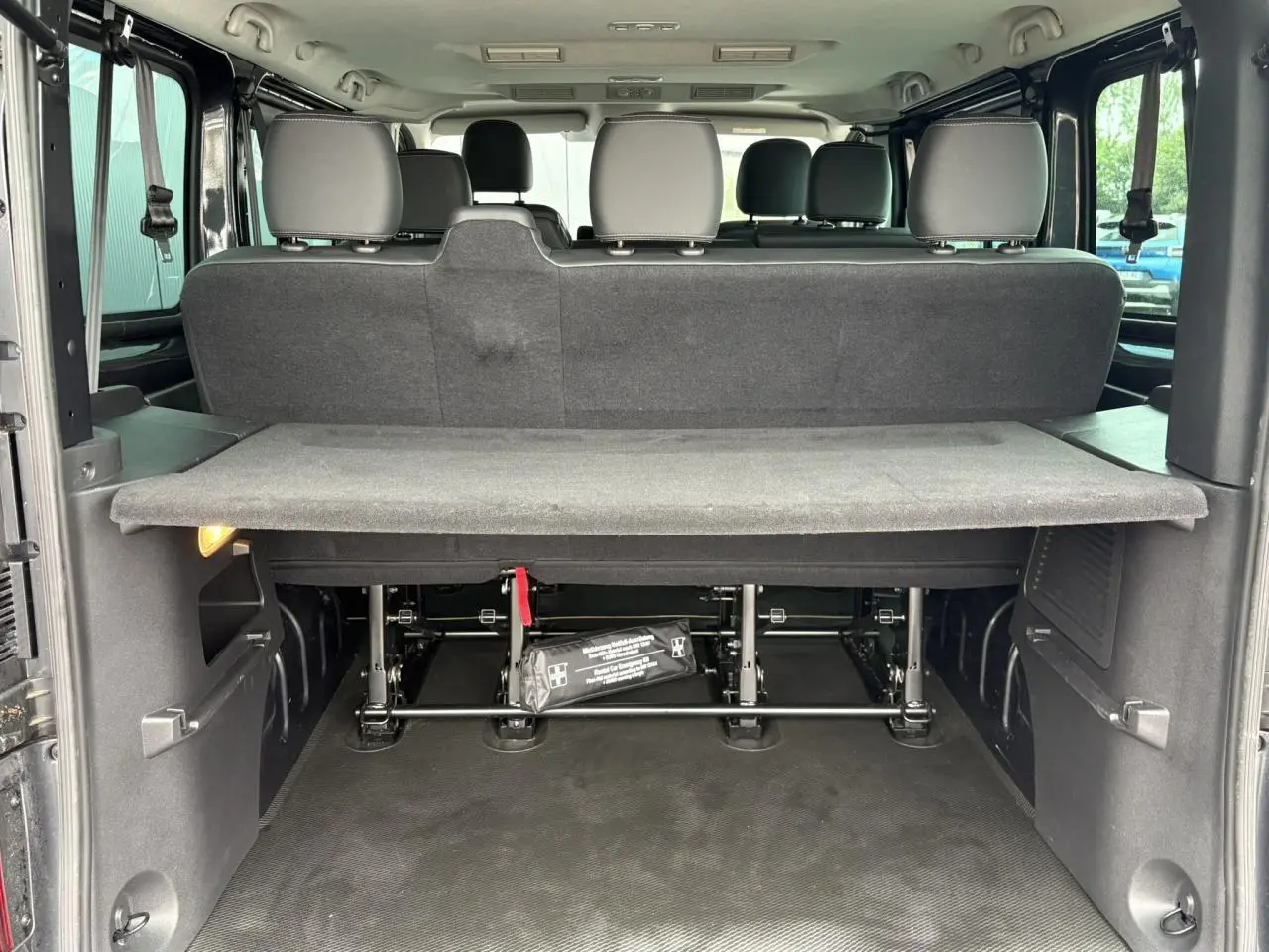 Vue arrière du coffre ouvert du Nissan Primastar gris, montrant la tablette cache-bagages et les sièges arrière.