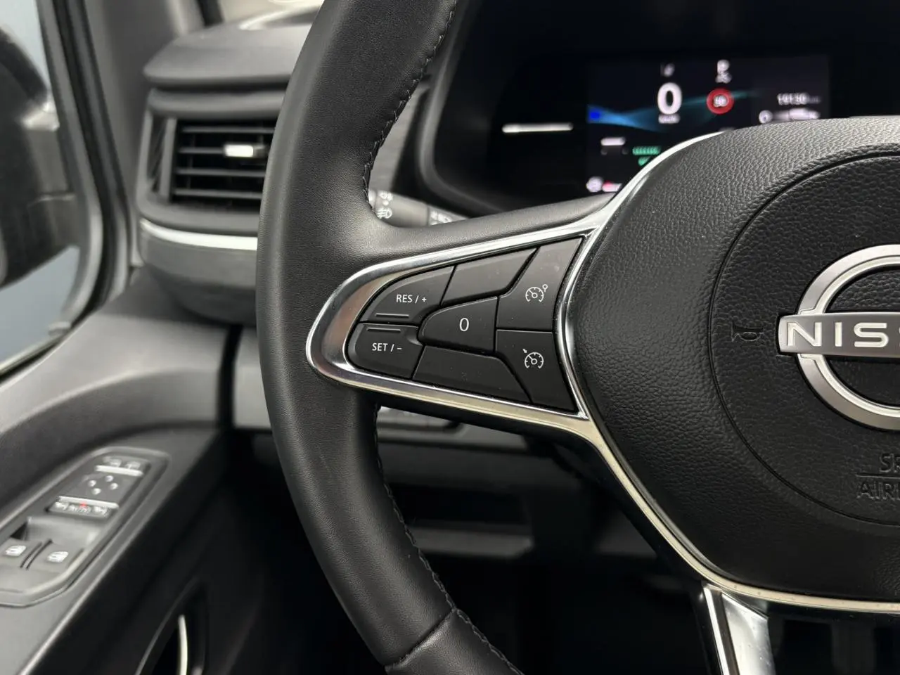 Vue rapprochée du volant noir du Nissan Primastar 2025 avec commandes au volant et tableau de bord numérique flou.