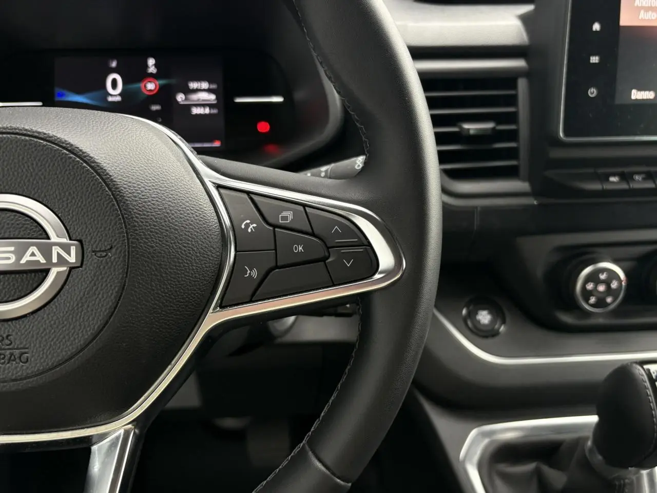 Gros plan sur le volant noir et la console centrale du Nissan Primastar 2025, avec commandes au volant et écran tactile visible.