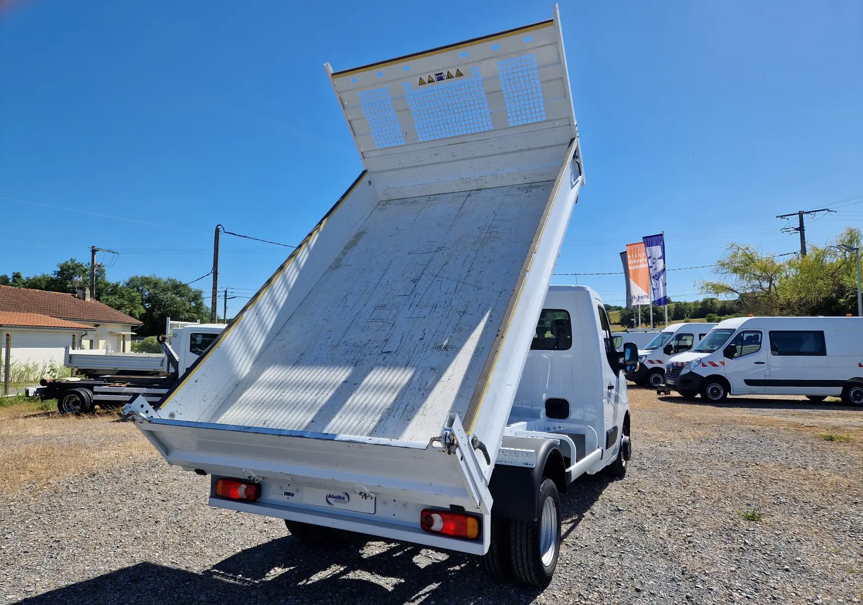 Vue 3/4 arrière droite d’un Renault Master Châssis Cabine blanc avec benne relevée sur un terrain extérieur.