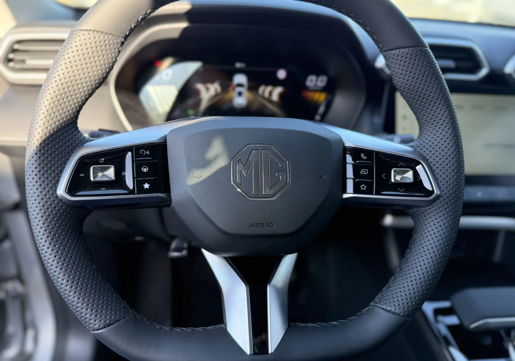 Vue rapprochée du volant en cuir perforé noir du MG ZS 1.5 L Hybrid+ 197 ch, avec commandes intégrées et logo MG central.