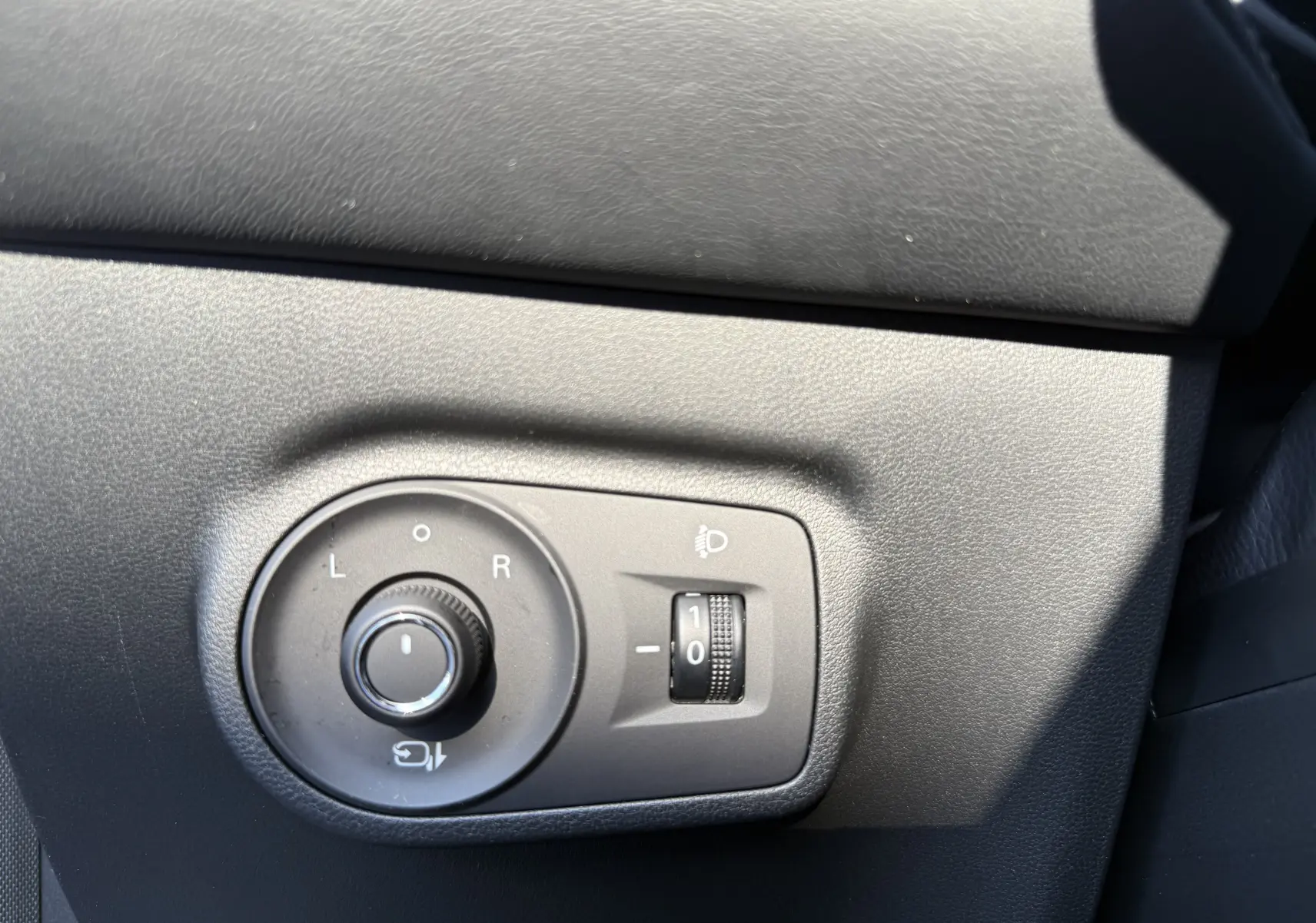 Gros plan sur les commandes de réglage des rétroviseurs et des phares du MG ZS 1.5 L Hybrid+ Luxury en gris Hampstead.