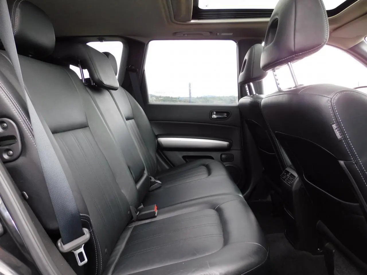 Vue latérale intérieure des sièges arrière en cuir noir du Nissan X-TRAIL 2011 avec toit ouvrant panoramique.