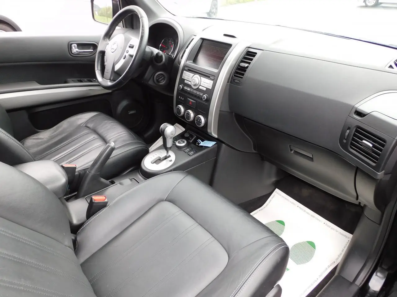 Intérieur noir cuir du Nissan X-TRAIL 2011 vu côté passager, avec tableau de bord et console centrale visibles.