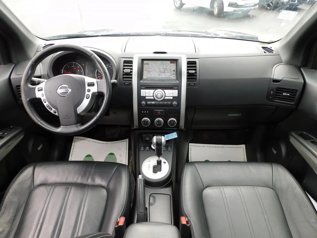 Vue intérieure avant du Nissan X-TRAIL noir de 2011, montrant tableau de bord, volant cuir et console centrale avec écran GPS.