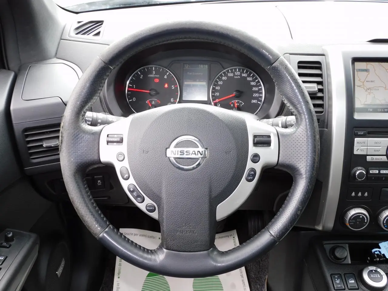 Vue rapprochée du volant Nissan X-TRAIL 2011 avec commandes intégrées et tableau de bord visible en arrière-plan.