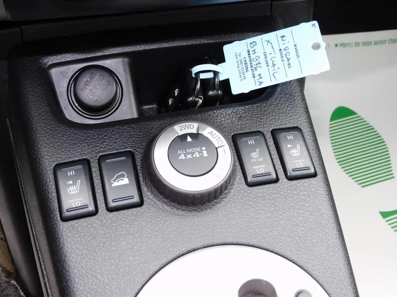 Gros plan sur la console centrale noire du Nissan X-TRAIL 2011, montrant les commandes 4x4 et sièges chauffants.