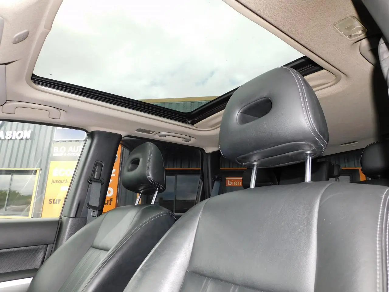 Vue intérieure du Nissan X-TRAIL 2011 montrant les sièges avant en cuir noir et le toit ouvrant panoramique.