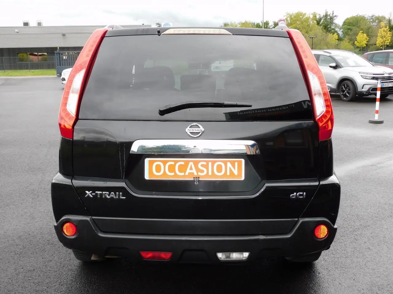 Vue arrière d'un Nissan X-Trail noir avec feux rouges verticaux et plaque "OCCASION" orange visible.