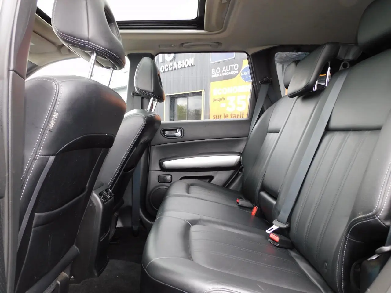Vue latérale intérieure du Nissan X-TRAIL 2011, sièges arrière en cuir noir sous toit ouvrant panoramique.