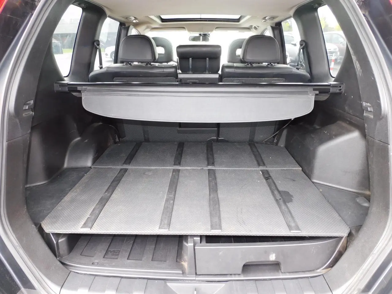 Coffre ouvert du Nissan X-TRAIL noir 2011, montrant le Flexiboard® à deux niveaux avec cache-bagages enrouleur.