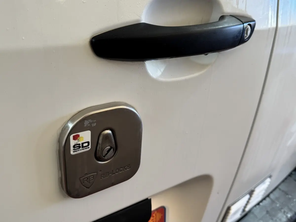 Gros plan sur la serrure antivol argentée et la poignée noire de la porte côté droit du Citroën Berlingo blanc.