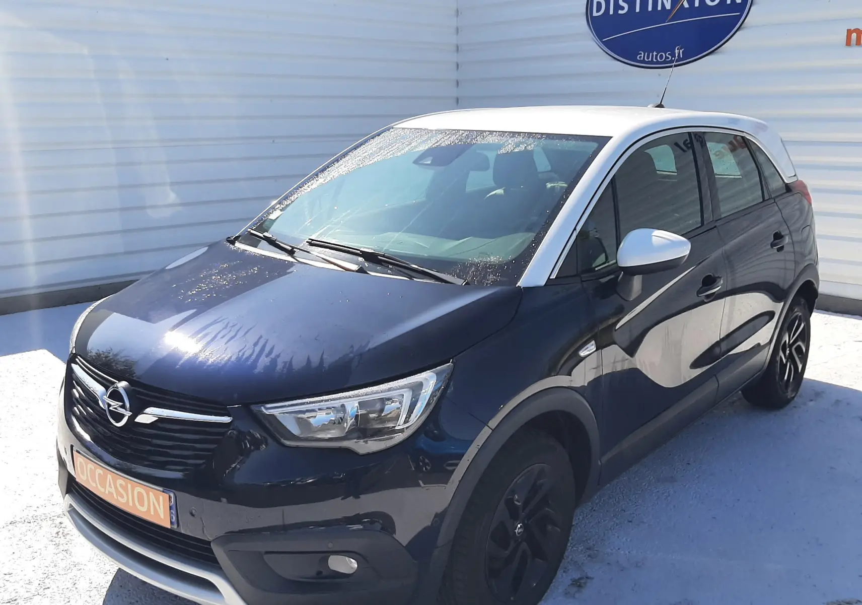 Opel Crossland X 130ch Innovation noir avec toit blanc, vue 3/4 avant droit, stationné devant un mur blanc.