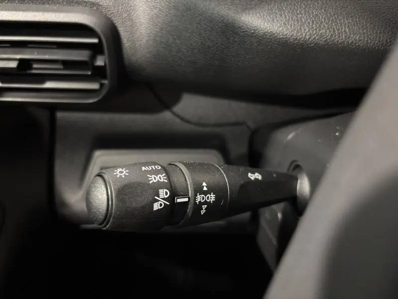 Gros plan sur la commande des phares du Peugeot Partner blanc Icy, côté gauche du volant, intérieur noir.