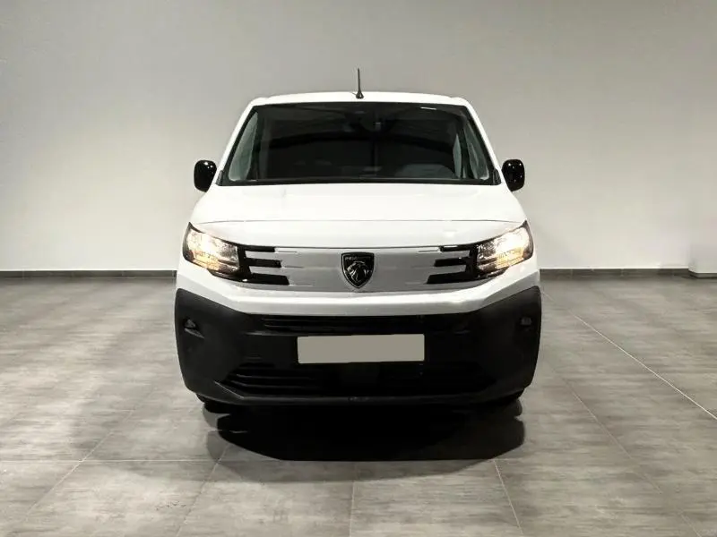 Vue frontale d'un Peugeot Partner XL blanc Icy avec phares allumés dans un espace intérieur neutre.