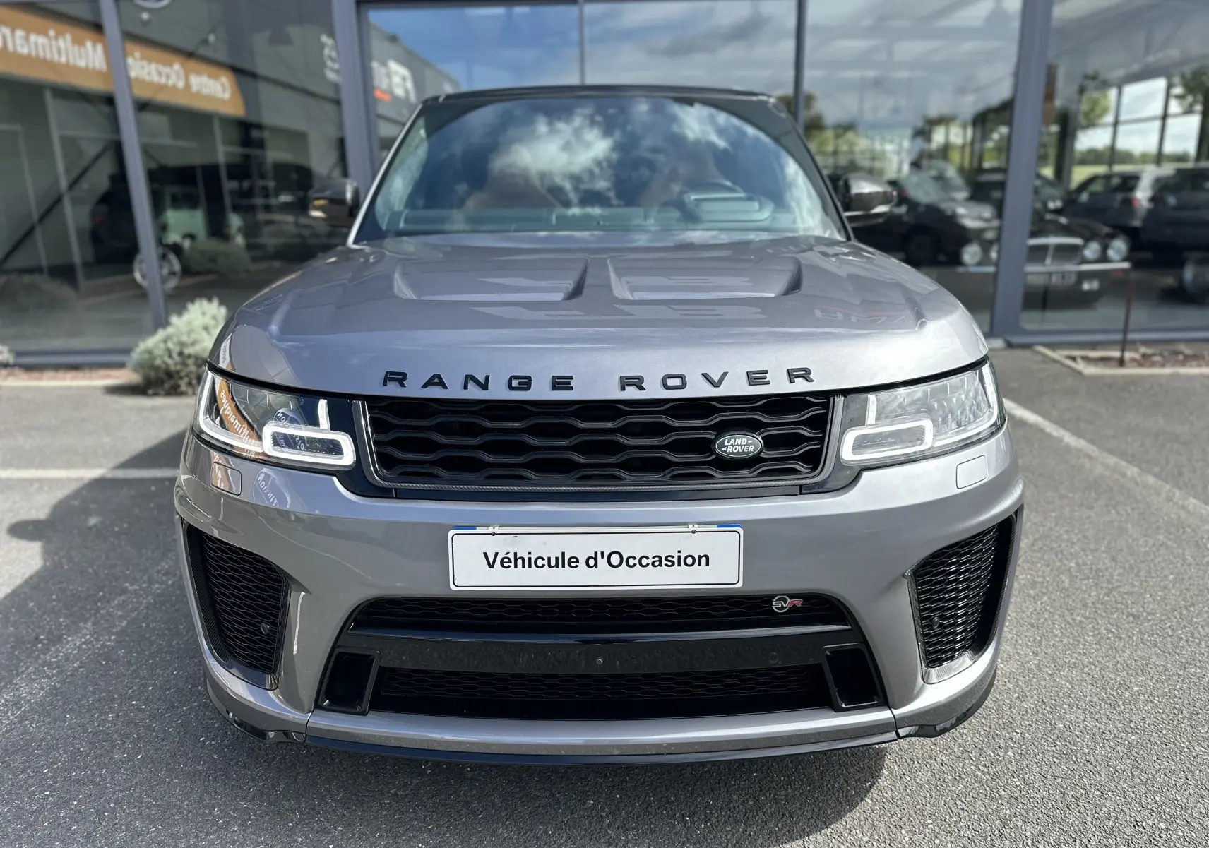 Vue frontale d'un Range Rover Sport gris foncé avec calandre noire et phares LED distinctifs, devant un showroom.