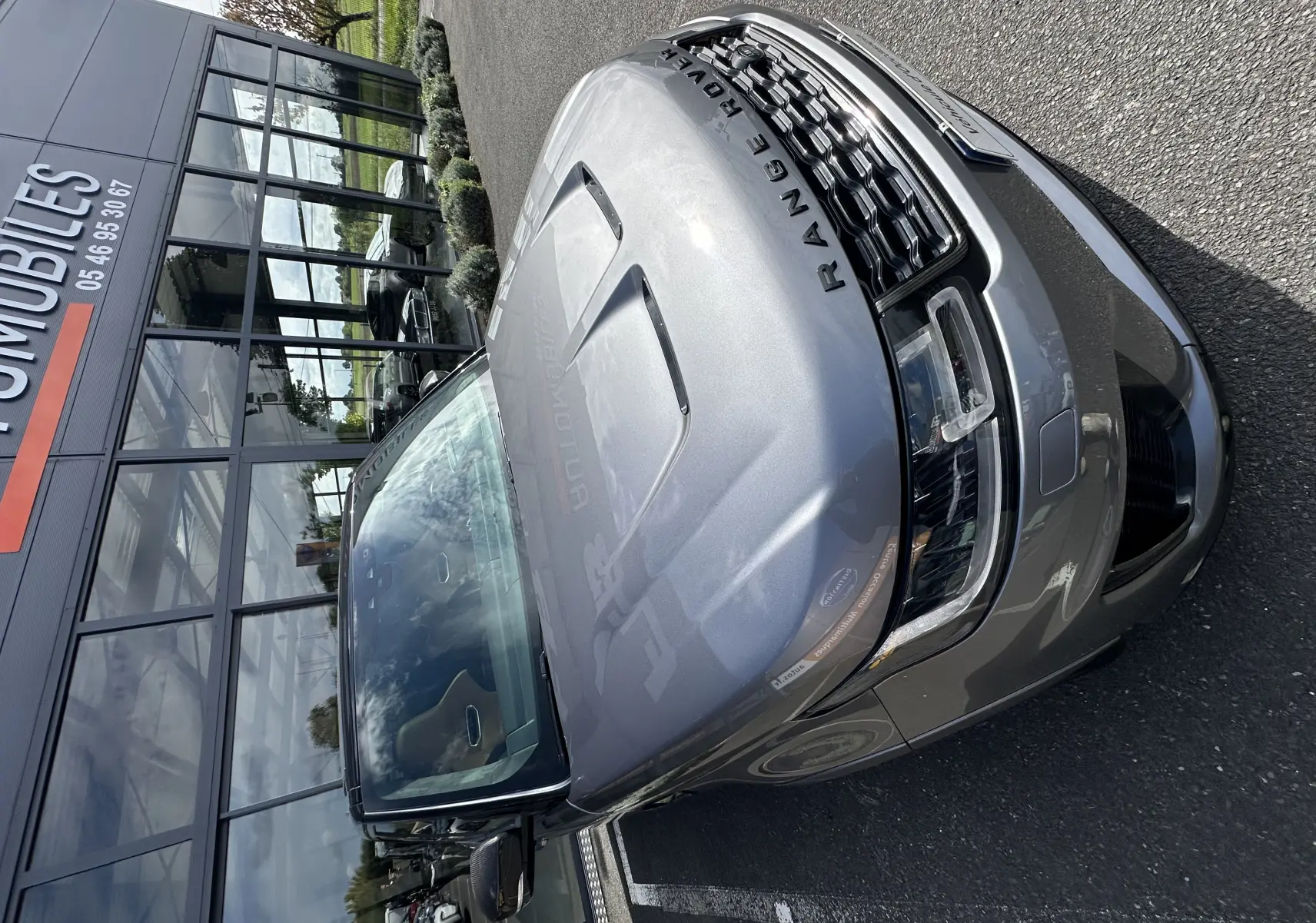 Vue 3/4 avant droit d'un Range Rover Sport SVR Carbon Edition gris foncé garé devant un bâtiment vitré.