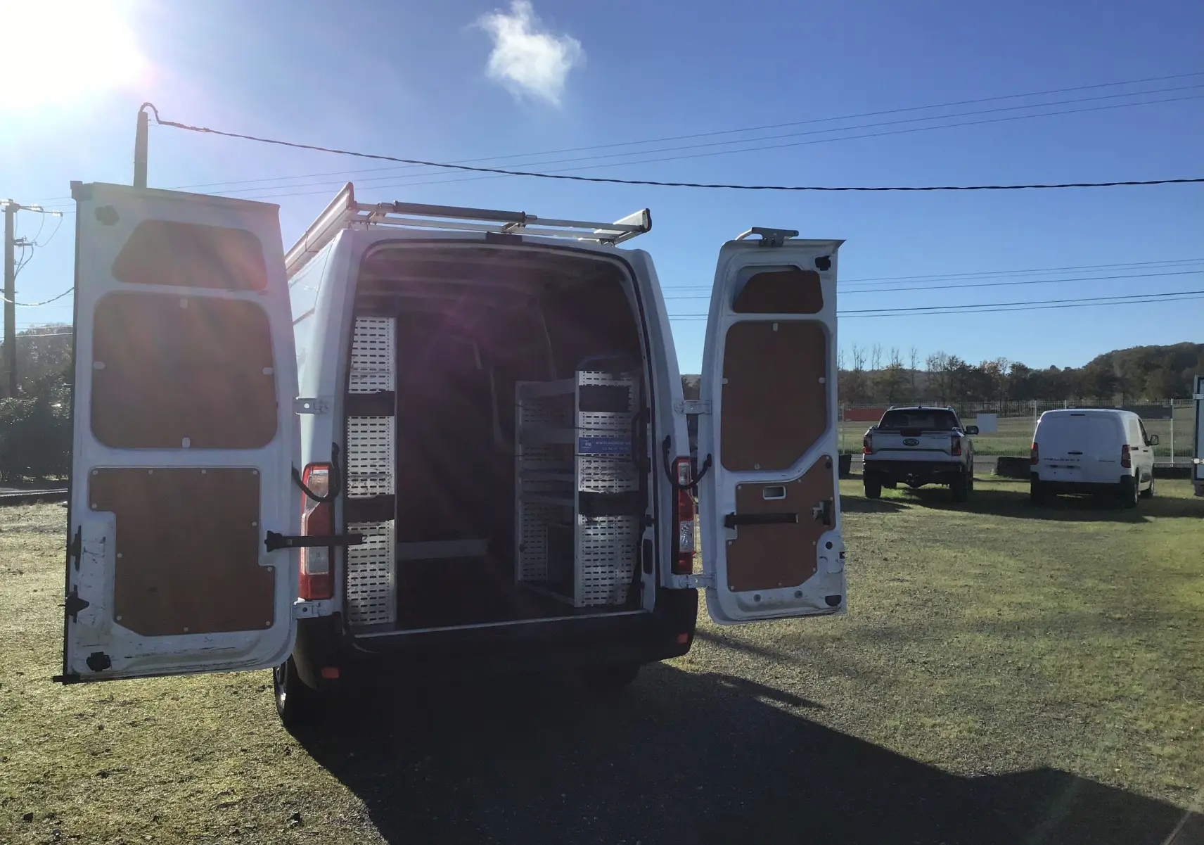 Vue arrière du Renault Master blanc L2H2 2020 avec portes ouvertes montrant l'aménagement intérieur en étagères métalliques.
