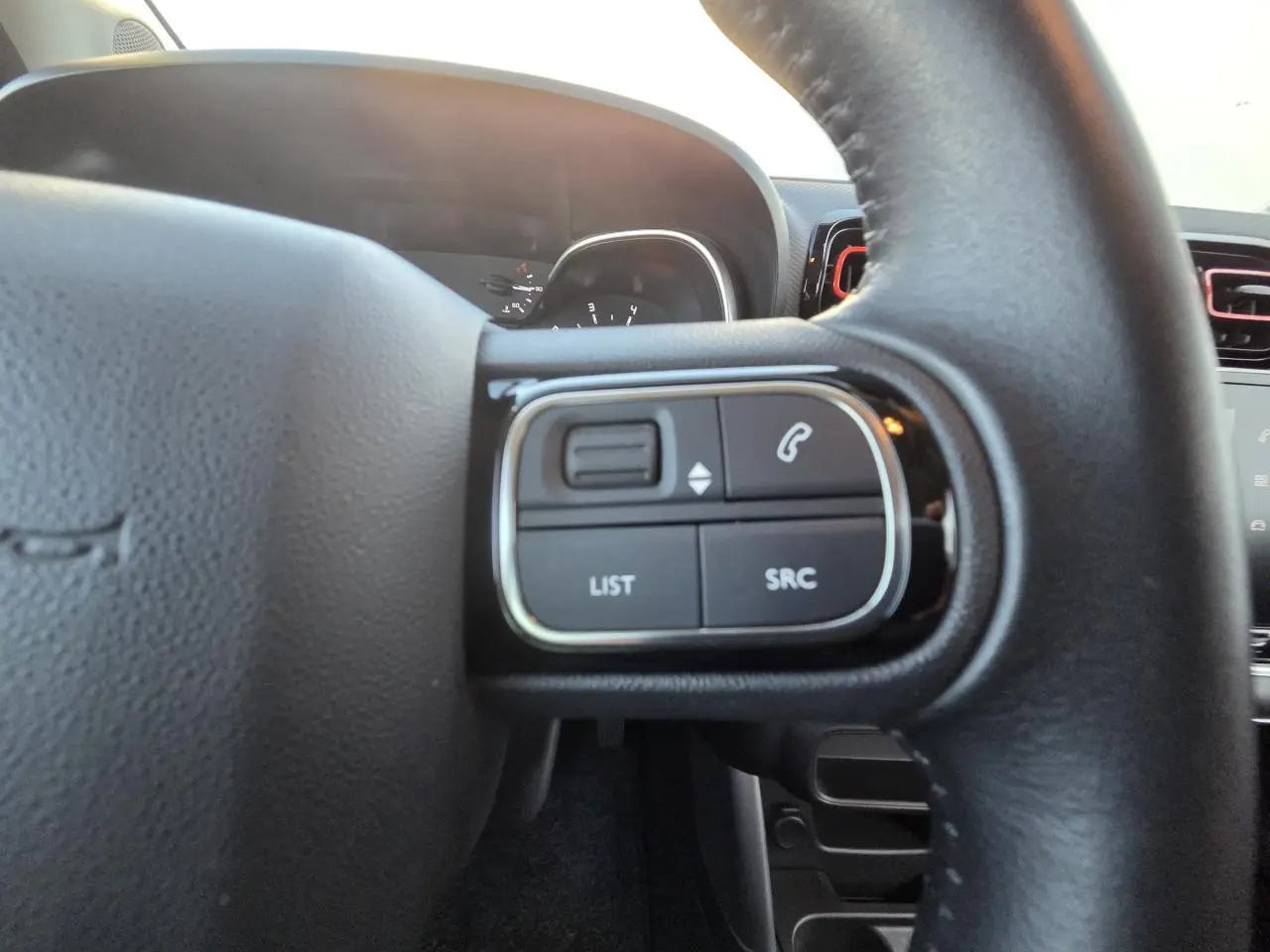 Gros plan sur les commandes audio au volant en cuir noir de la Citroën C3 Aircross 2021, tableau de bord en arrière-plan.