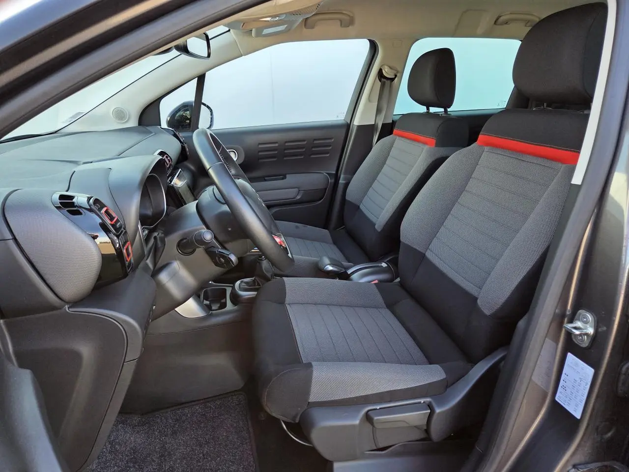 Intérieur avant droit de la Citroën C3 Aircross 2021 avec sièges tissu gris et bande rouge, volant et tableau de bord visibles.