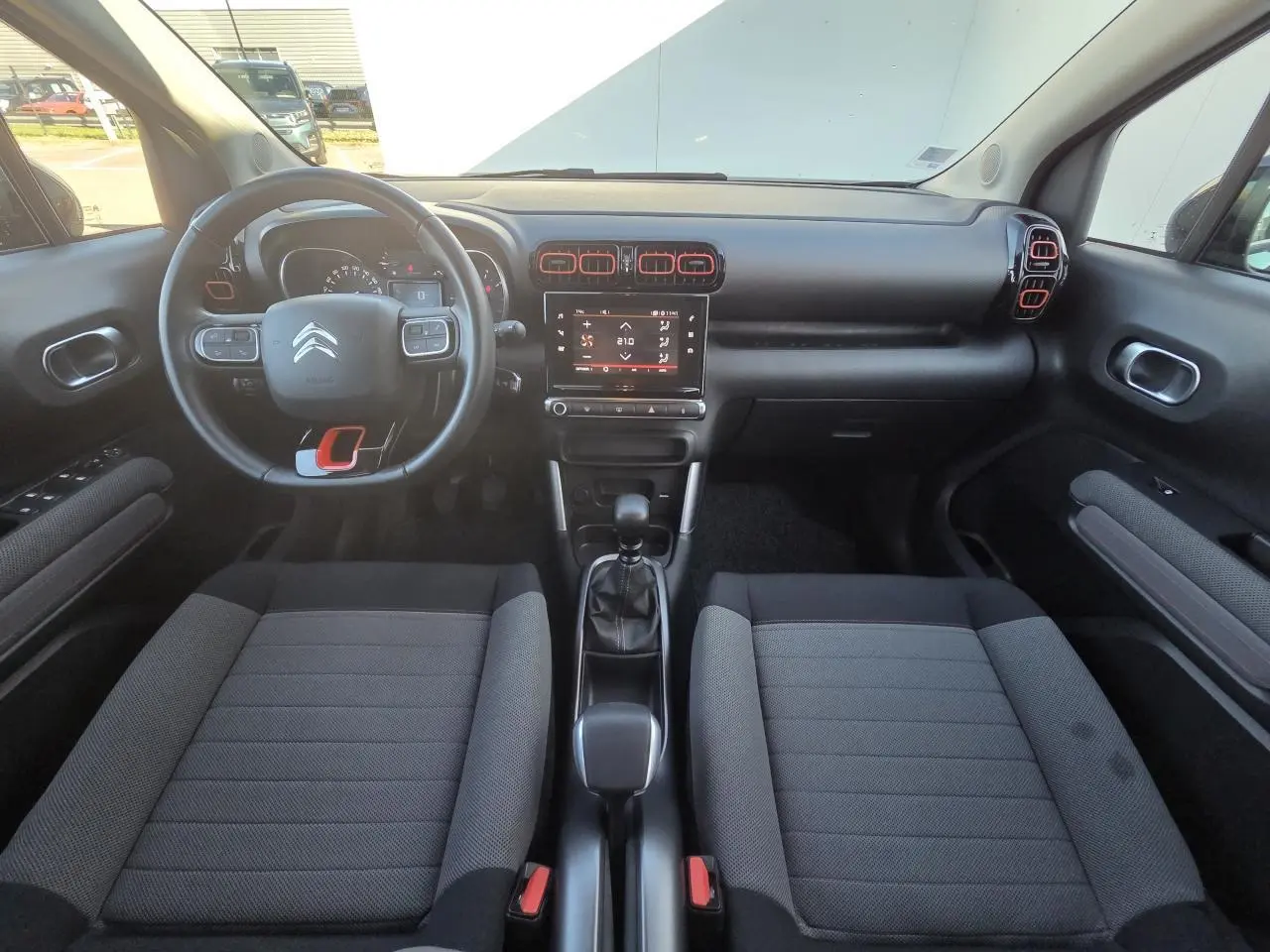Intérieur avant du Citroën C3 Aircross 2021, tableau de bord noir avec touches rouges et sièges tissu gris foncé.