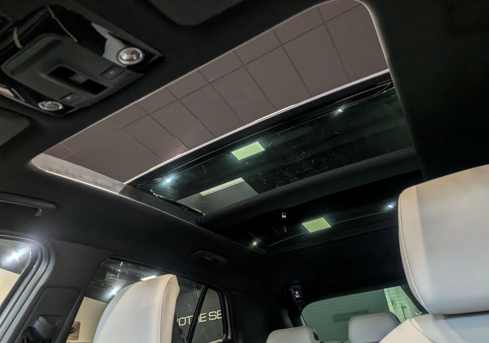 Vue intérieure du toit ouvrant panoramique du Kia Sportage 2025 gris céramique avec sièges cuir clair et plafond noir.