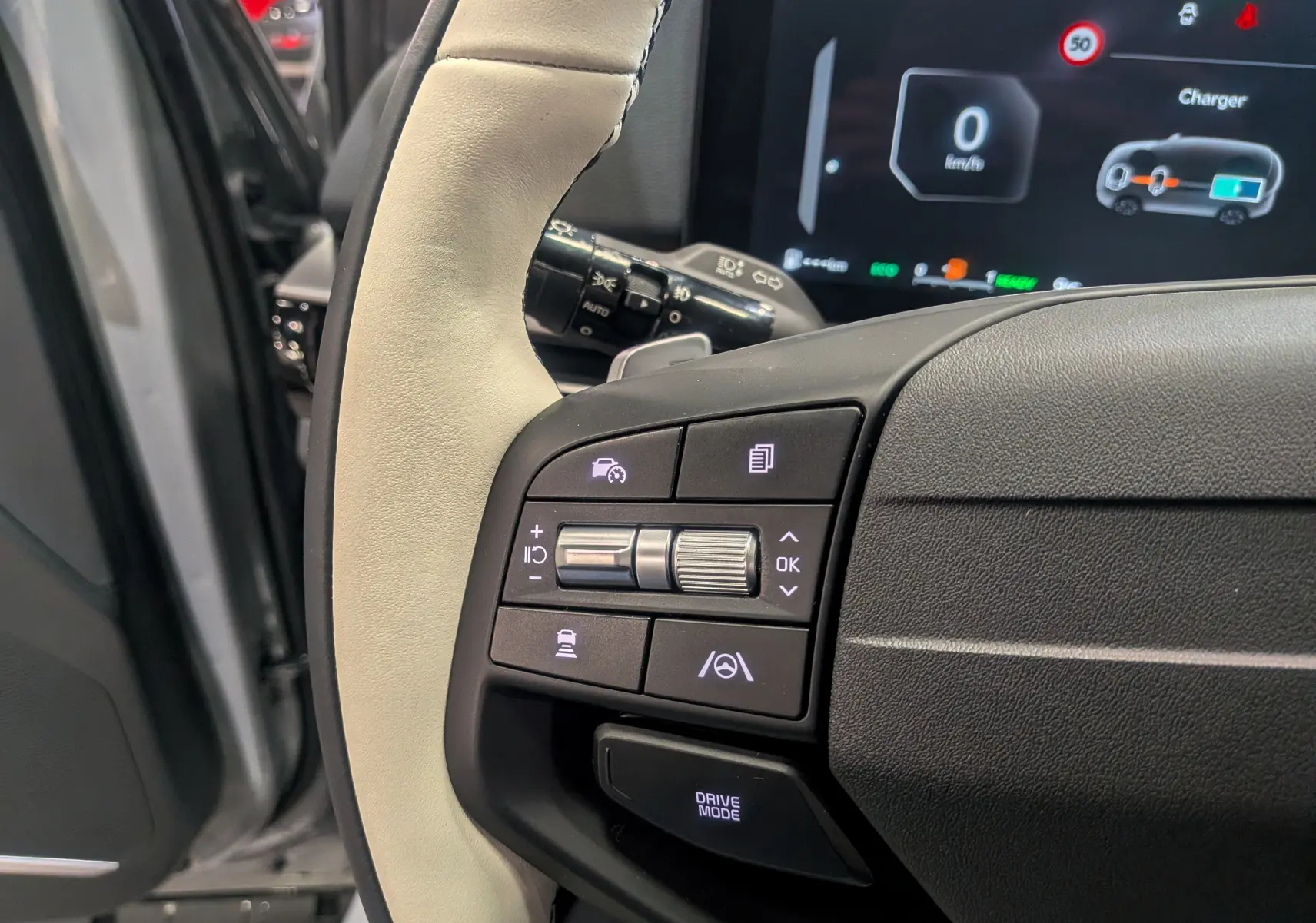 Gros plan sur le volant cuir clair du Kia Sportage 2025 avec commandes intégrées et tableau de bord numérique en arrière-plan.