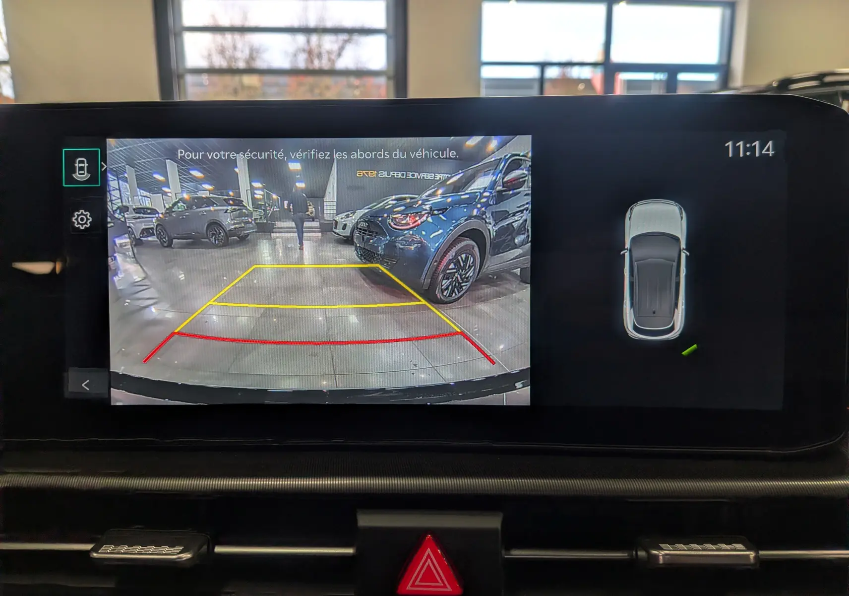Vue caméra de recul montrant un Kia Sportage gris céramique avec toit noir dans un showroom lumineux.