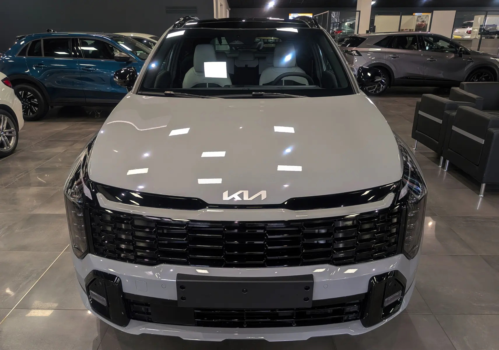 Vue frontale d'un KIA SPORTAGE 2025 gris céramique avec toit noir et calandre noire brillante en showroom.