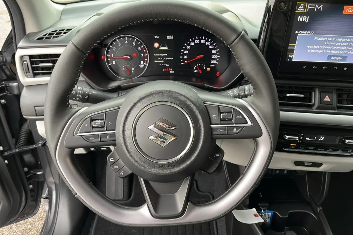 Vue intérieure centrée sur le volant cuir multifonctions d'une Suzuki Swift gris minéral avec tableau de bord et écran tactile.