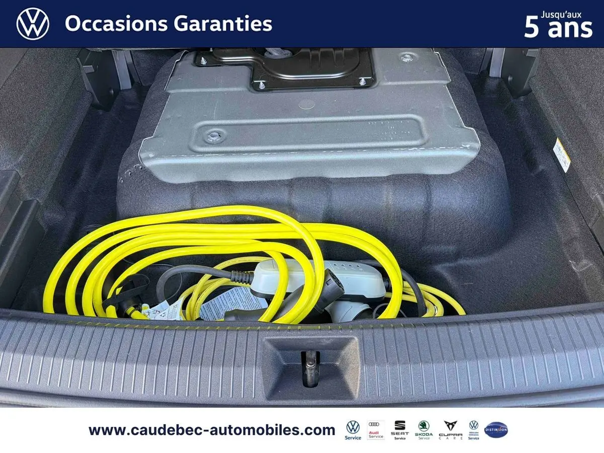 Coffre ouvert d’un Volkswagen Tiguan argent Dolomite avec câble de recharge électrique jaune visible.