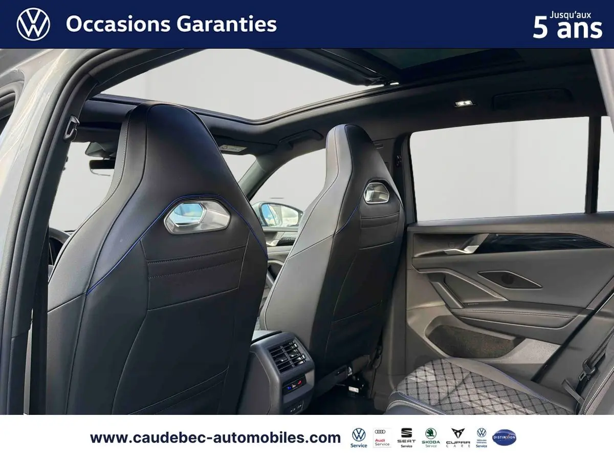 Vue intérieure arrière du Volkswagen Tiguan eHybrid 2025, sièges sport noirs avec surpiqûres bleues et toit ouvrant panoramique.