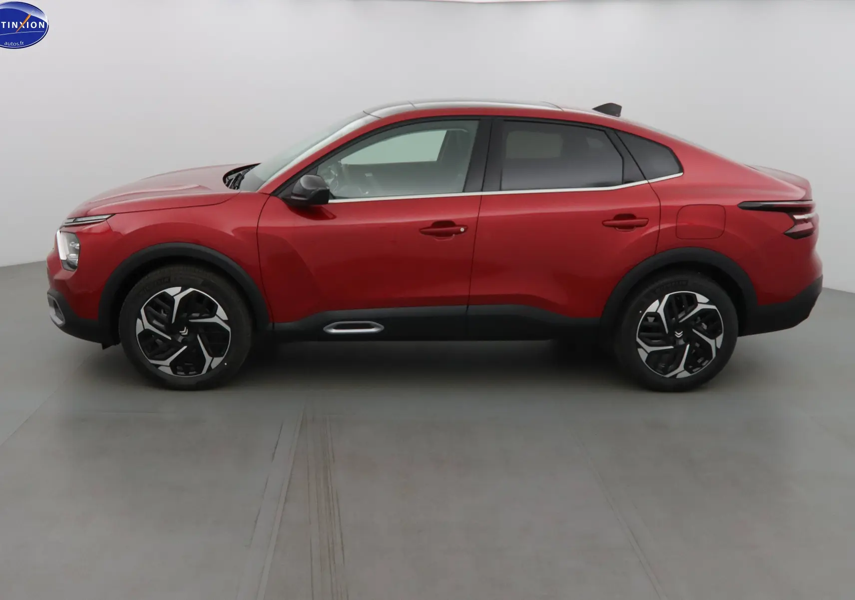 Profil côté gauche d'une Citroën C4 X rouge Elixir métal 2023 avec jantes bicolores et toit noir contrasté.