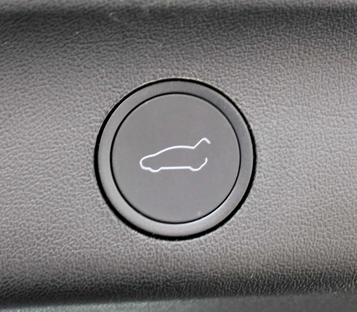 Bouton noir avec icône blanche de hayon ouvert, détail intérieur du Tesla Model Y noir métal 2024.