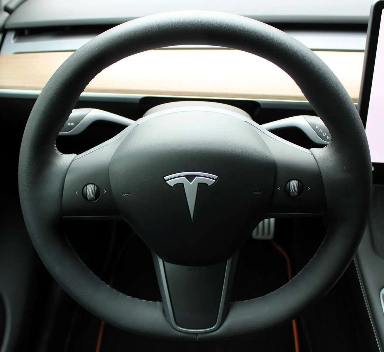 Gros plan sur le volant noir de la Tesla Model Y 2024 avec tableau de bord en bois clair en arrière-plan.