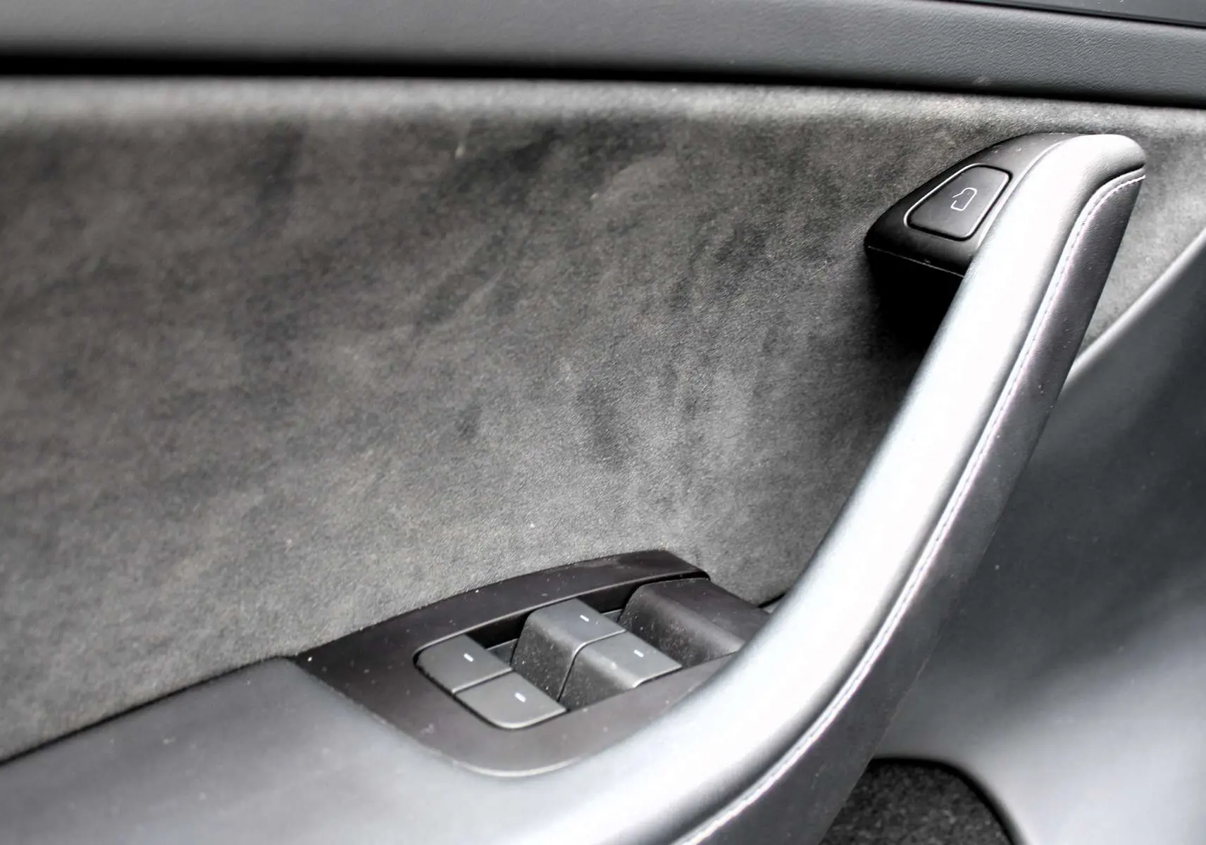 Détail de la poignée intérieure côté gauche en cuir noir et commandes de vitres de la Tesla Model Y Performance 2024.