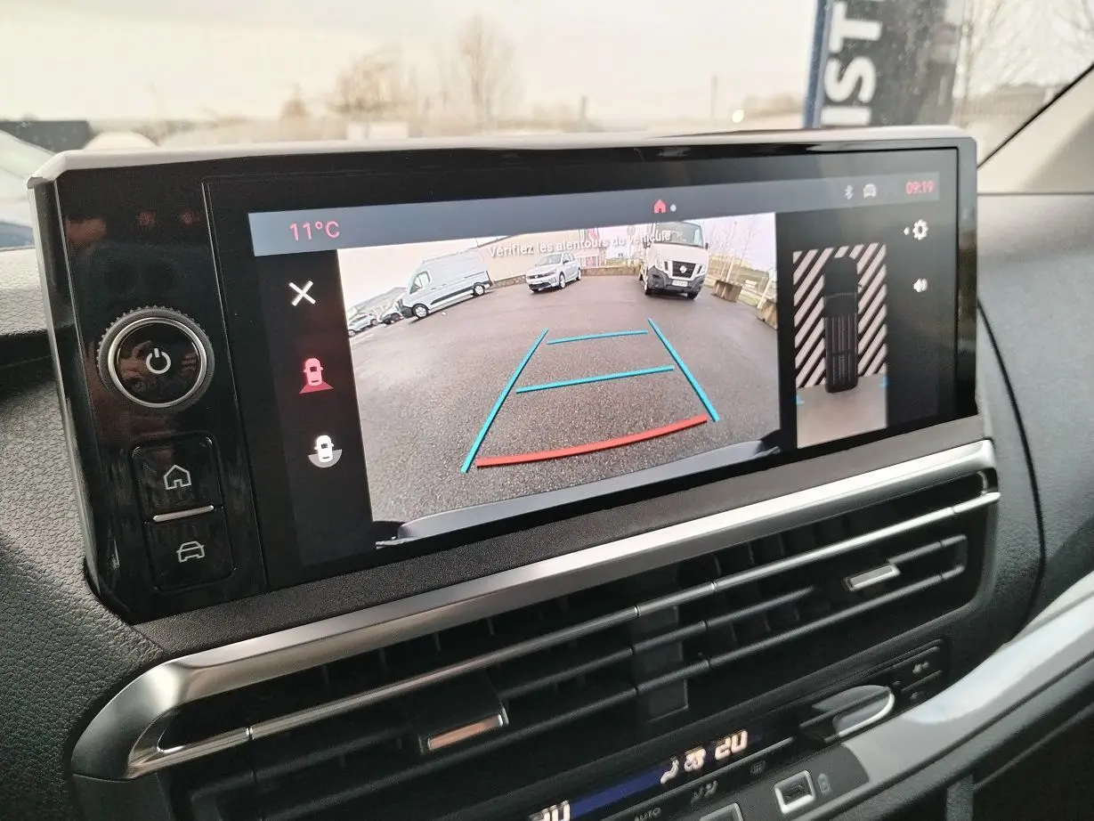 Écran central du tableau de bord montrant la caméra de recul avec vue arrière sur un parking, intérieur noir.